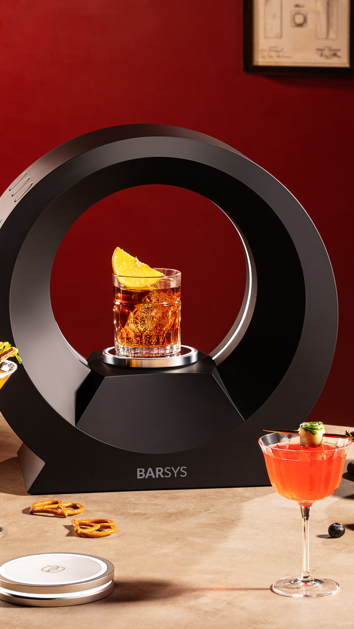 A Barsys 360 with a garnished whiskey cocktail against a red wall.