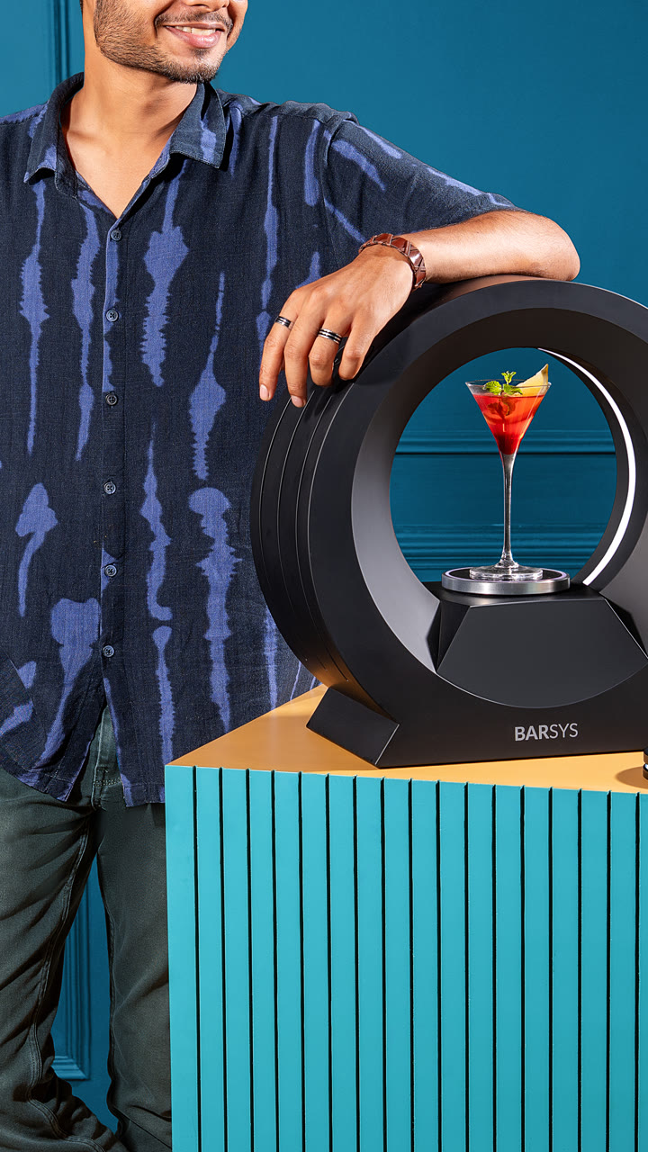 A guest leans on a Barsys 360 holding a garnished cocktail.