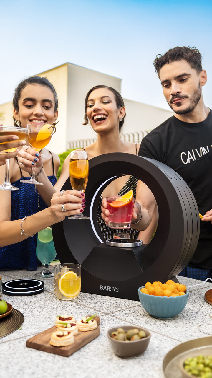 Three friends toast beside a Barsys 360 at an outdoor table.