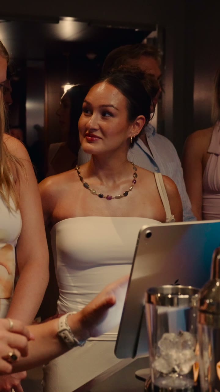 A guest in white chooses her drink on the tablet beside the Barsys 360, from the NYC event film.