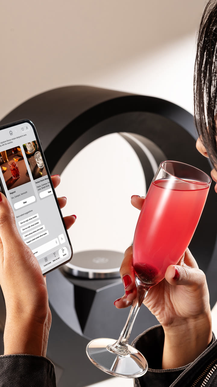 A guest holds a pink cocktail and the Barsys app beside the 360.